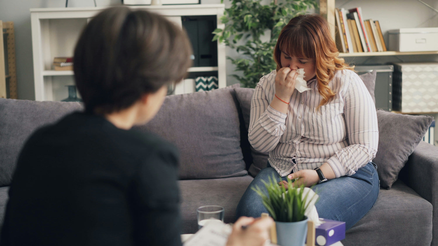 Women sitting on a couch sneezing into a tissue